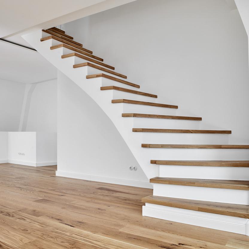 Schwebende Treppe nach Maß in einem modernen Wohnraum. Maßgefertigte, schwebende Holzstufen auf weißem Untergrund in einem hellen Raum, stilvoll und zeitgenössisch.