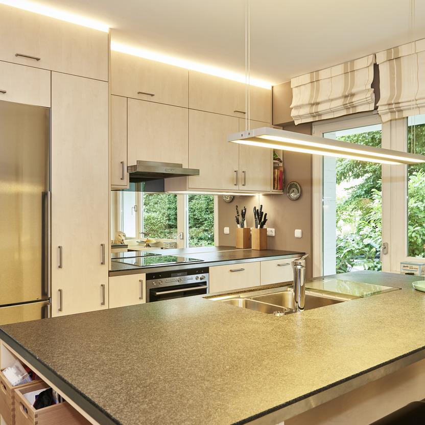 Maßgeschneiderte Küche in hellem Holzdekor mit modernen Geräten und großem Fenster mit Gartenblick.