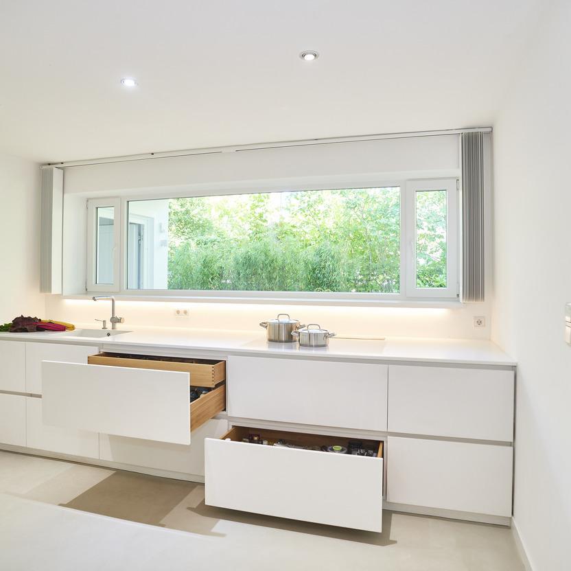 Maßgefertigte, weiße Küchenschränke mit offenen Schubladen, die eine effiziente Raumnutzung in einer modernen Küche zeigen.