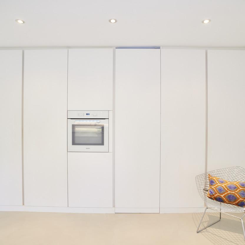 Elegante, weiße Küchenfront nach Maß mit eingebautem Ofen und einem Designerstuhl als Akzent.