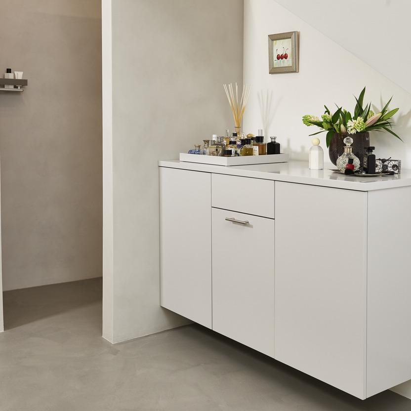 Stilvolles Sideboard nach Maß in Weiß, aufgeräumt mit Duftstäbchen und Pflanze, unter einer schrägen Wand in einem modernen Raum.