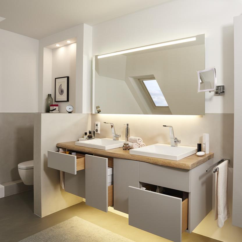 Ein modern gestaltetes Badezimmer mit zwei eingelassenen Waschbecken, maßgefertigten Badmöbeln in Holzoptik und weißen Fronten, sowie einem beleuchteten Spiegel und einem Dachfenster.